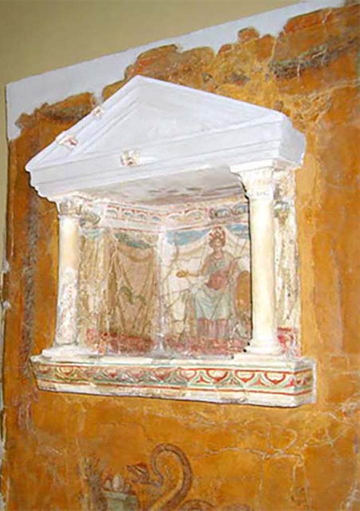 Gragnano, Villa rustica in Località Carmiano, Villa A. Lararium niche.
From dividing pilaster between kitchen room 4 and room 2.
Lararium in stucco found inserted in a yellow painted wall.
The lararium had a triangular pediment supported by two Corinthian columns.
The painting at the rear showed an enthroned Minerva with breastplate, helmet, shield, lance in the left hand and gilded/golden plate in the right.