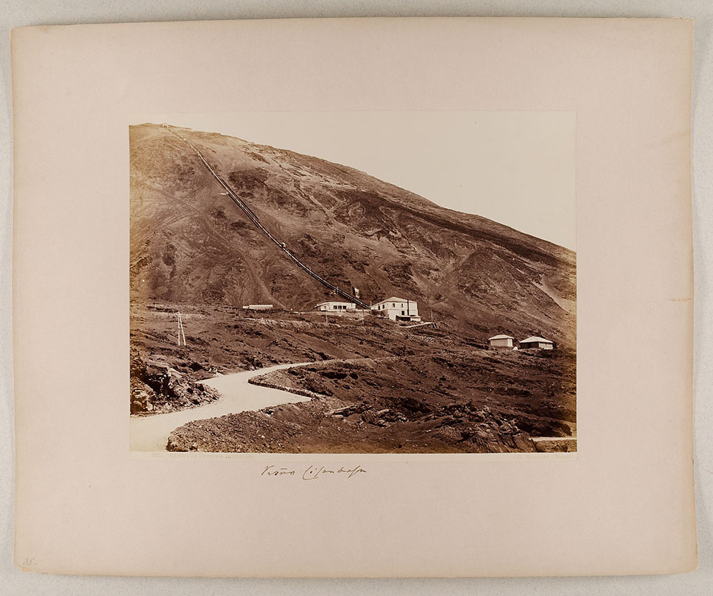 Vesuvius Funicular railway. 1880-1890 photo of the lower station and the track up to the summit.
Photo title at bottom is "8121 Vesuvio. Ferrovia funicolare. G. Sommer – Napoli”.
The handwritten note says "Vesuv Eisenbahn".
Museum für Kunst und Gewerbe Hamburg, inventory number P1981.400 (Public Domain).
See https://sammlungonline.mkg-hamburg.de/de/object/8121-Vesuvio.-Ferrovia-funicolare/P1981.400/mkg-e00135742