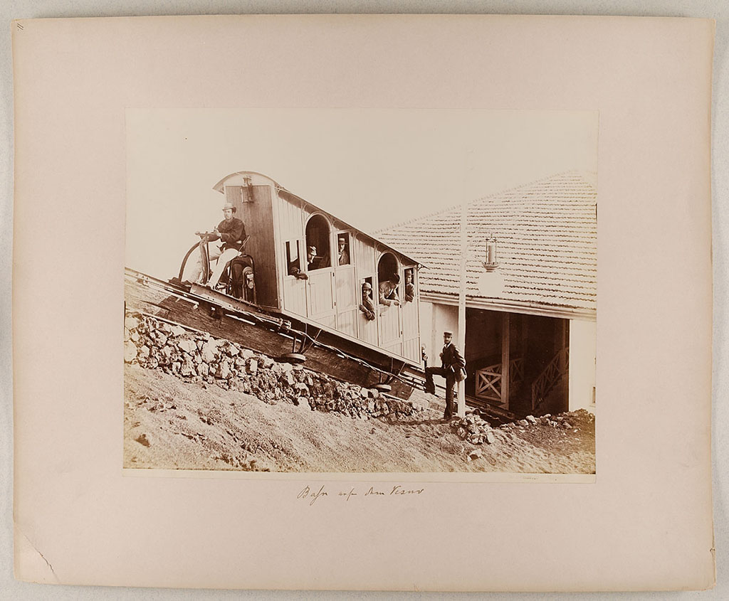 Vesuvius Funicular railway. An original 1880 car at the lower station, 1880-1889.
Photo title at bottom is 8124 Vesuvio Stazione inferiore, G. Sommer Napoli.
The handwritten note says “Bahn auf den Vesuv”.
Museum für Kunst und Gewerbe Hamburg, inventory number P1981.399 (Public Domain).
See https://sammlungonline.mkg-hamburg.de/de/object/8124-Vesuvio-Stazione-inferiore/P1981.399/mkg-e00135741