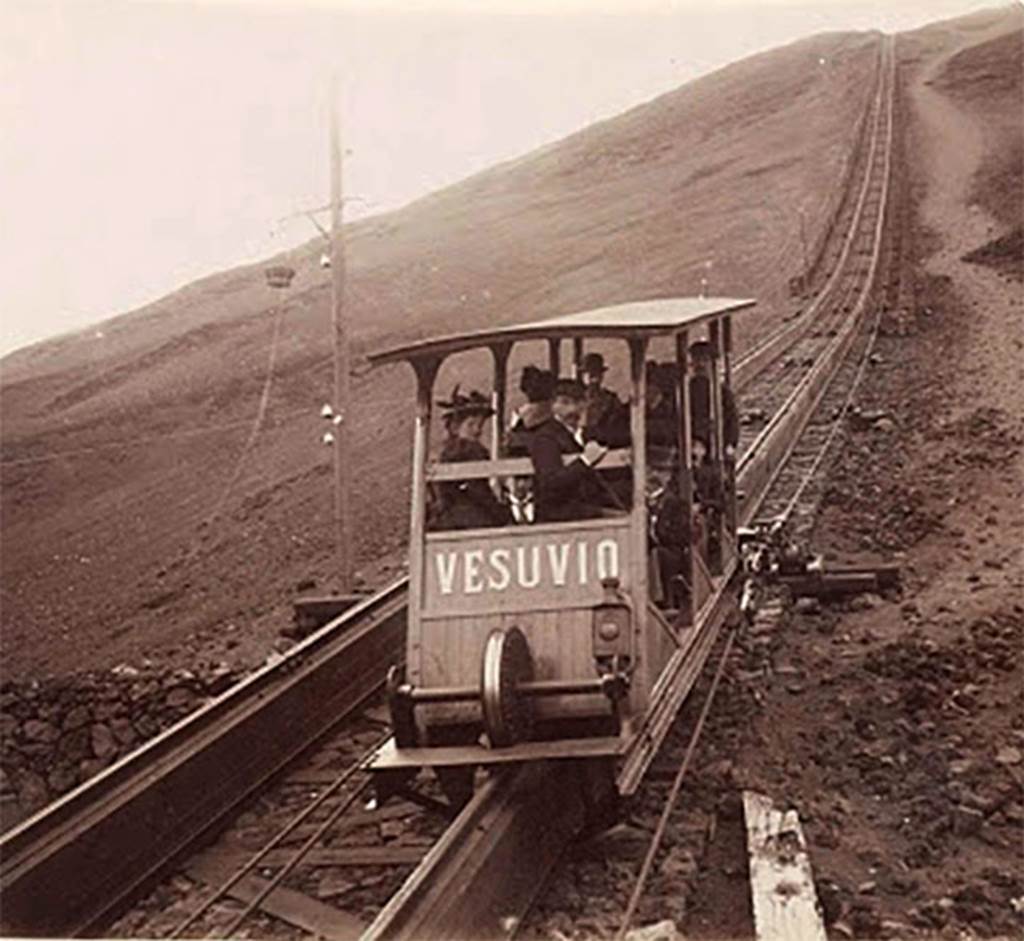 Vesuvius Funicular car Vesuvio. Undated black and white photo but must be between 1889 and 1904.
There was a longitudinal wooden sleeper on the top of which was carried a single rail.
The cars had a double flanged wheel at each end which ran on this rail.
In addition, there were two angled rails, one fixed to each side of the sleeper at its base.
The cars had wheels mounted from their floors which engaged on these side rails and kept the cars upright.
Each track had two continuous cables carried on pulleys which were fixed to each side of the car.