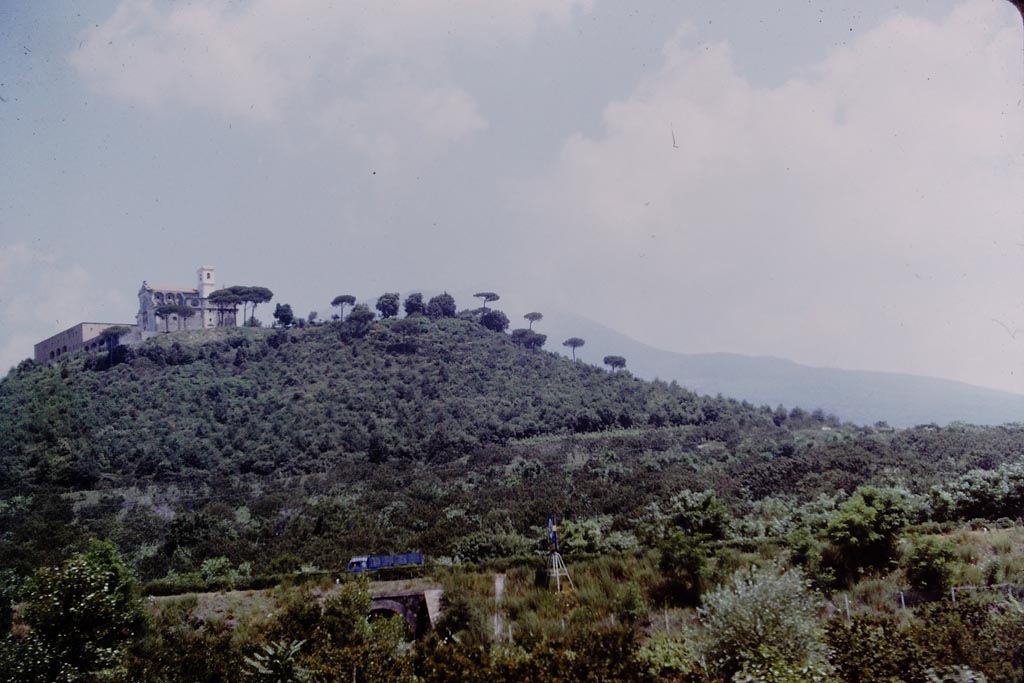 Missionari Redentoristi Colle Sant'Alfonso. 1964. Photo by Stanley A. Jashemski.
It sits on a hill of volcanic origin, S. Maria La Bruna, 185 metres high with Vesuvius behind to the north.
According to the church web site “the hill has suffered little from the devastating effects of nearby Vesuvius, from which a large valley separates it, enough to protect it from lava eruptions”.
The hill and church are a very prominent landmark to anyone travelling along the A3 autostrada who looks north towards Vesuvius.
Source: The Wilhelmina and Stanley A. Jashemski archive in the University of Maryland Library, Special Collections (See collection page) and made available under the Creative Commons Attribution-Non-commercial License v.4. See Licence and use details.
J64f1138